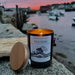 Lit Sea Hag candle by Rockport Candle Company on granite rocks with Rockport Harbor in the background 